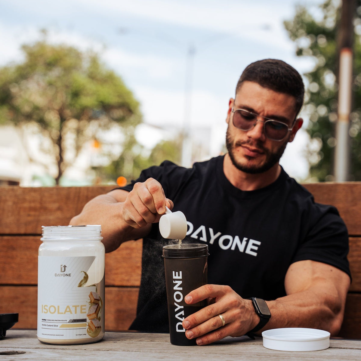 A man scooping ISOLATE Vanilla Custard Slice into a Day One shaker at an outdoor table